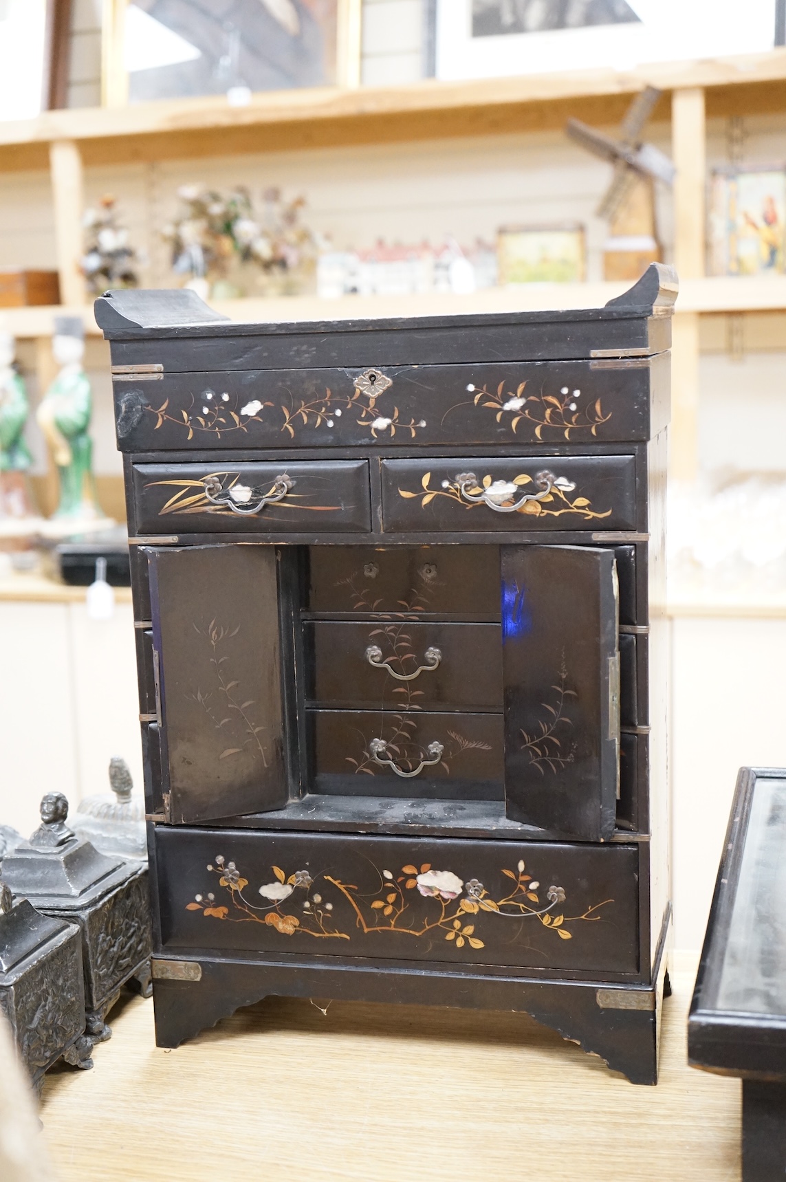 A Japanese lacquer table cabinet with inset porcelain panels, the drawers filled with sundry objects, clay pipes, decanter stoppers, etc, together with a black japanned wall clock, the dial inscribed F. L Hausburg, Paris